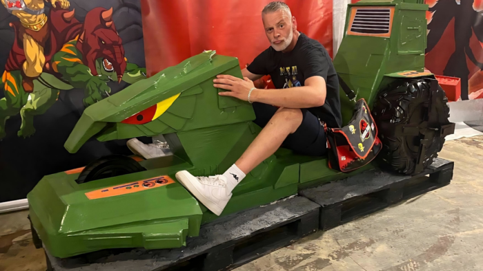 Ein Mann sitzt auf einem grünen Modell eines Alligator-Bikes aus dem Film 'Masters of the Universe'.